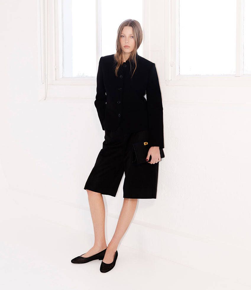 Woman wearing a black coat and black FIORA ballet flats against a white background