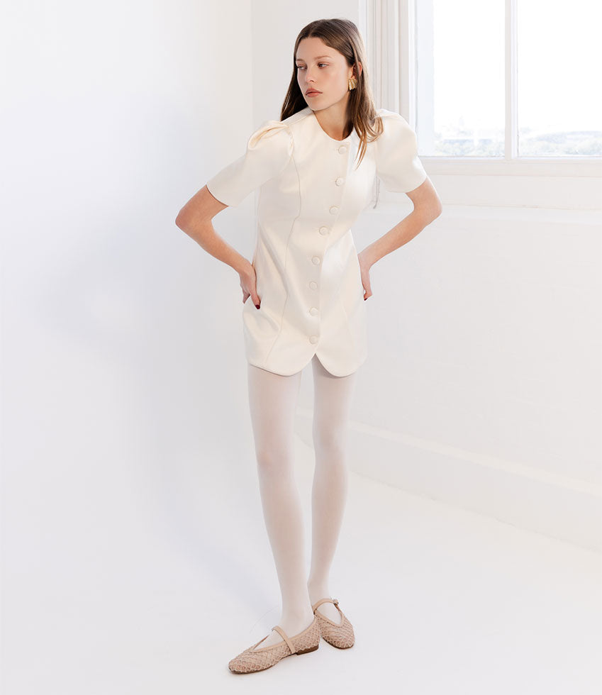 Woman wearing a white outfit with beige FLOSSY shoes in a minimalistic setting