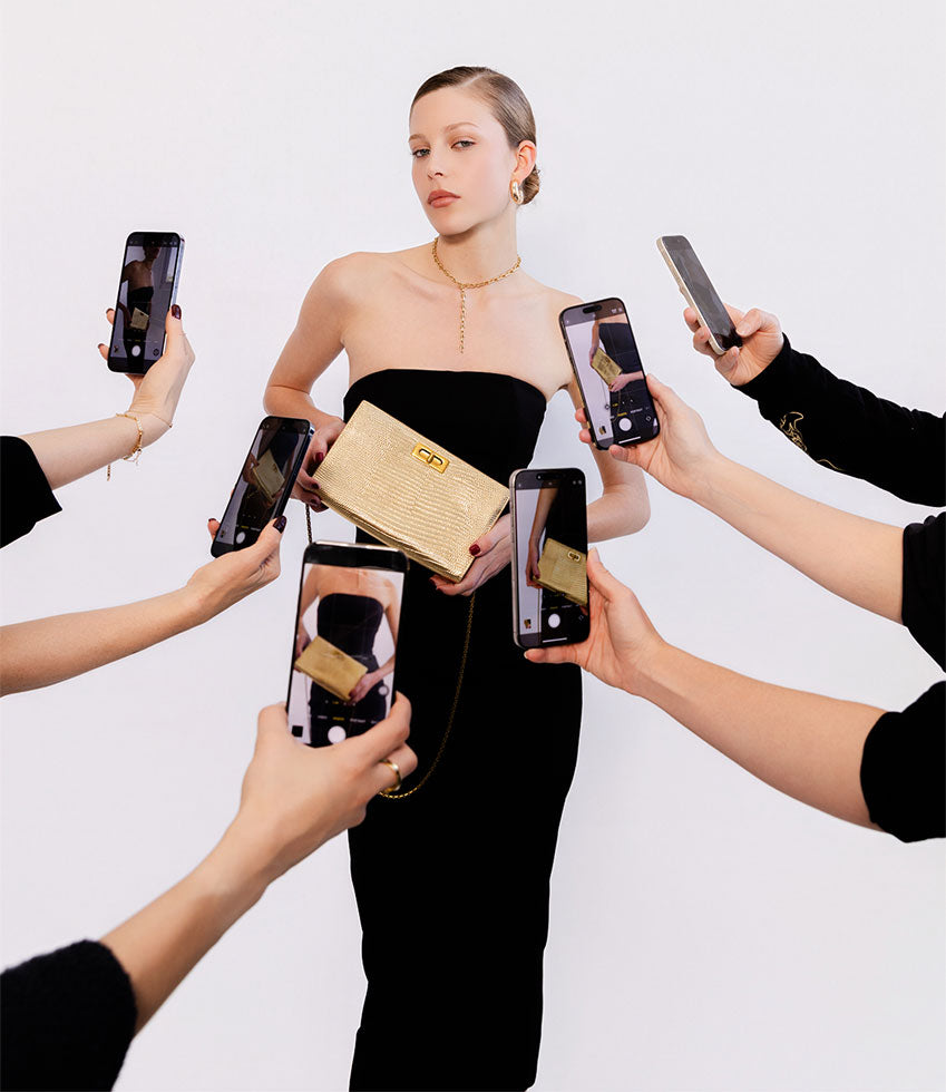 Woman holding a gold tejus NAYLA handbag with multiple hands holding smartphones around her