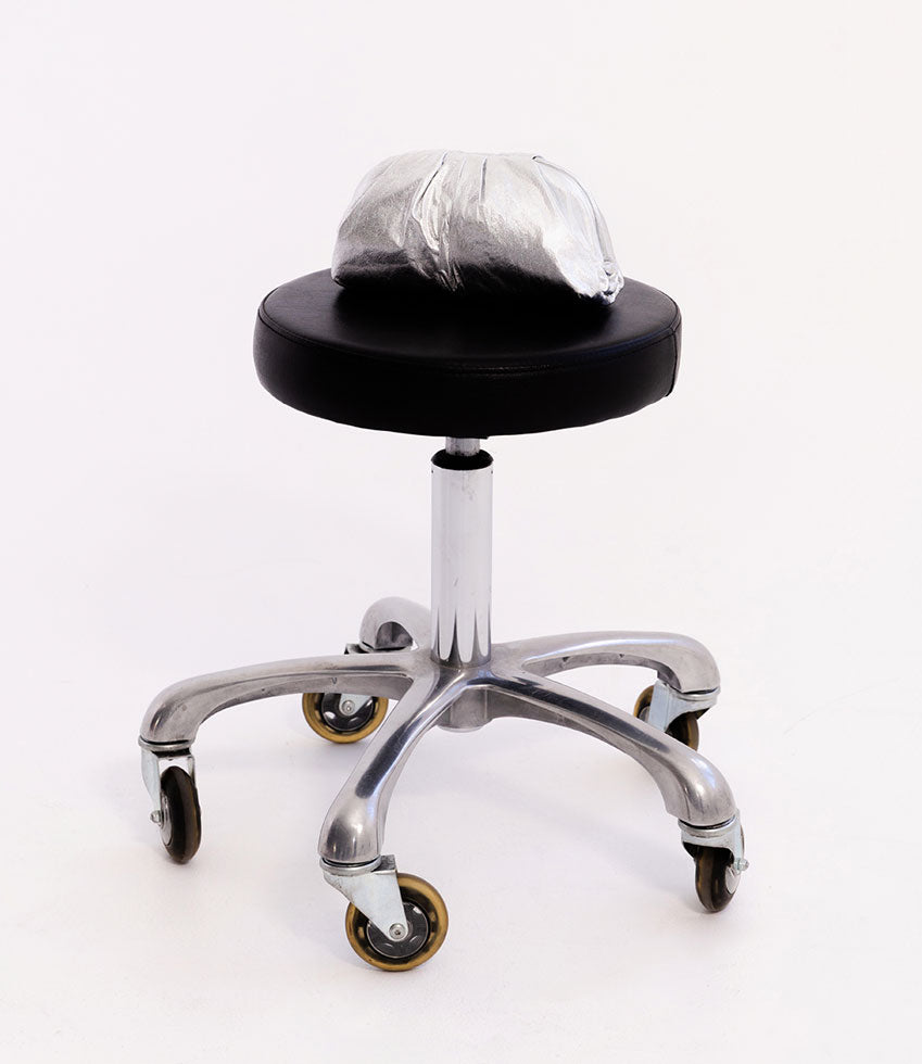 NEVA Ruched Frame Clutch in Silver on a stool with a black seat and chrome base on a white background
