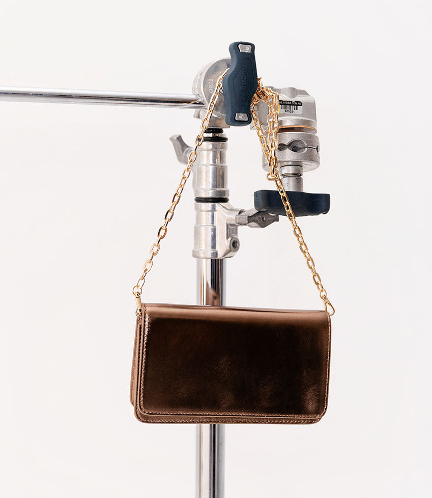 Bronze NYX leather handbag with a gold chain on a stand against a white background