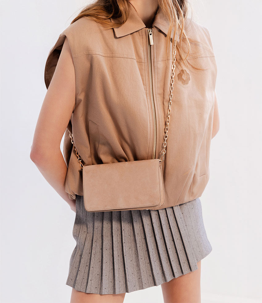 Person wearing a beige leather vest and carrying a sand suede NYX handbag on a white background