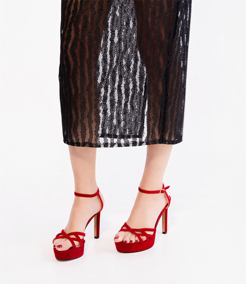 Red high-heeled shoes worn with a black sheer skirt on a white background
