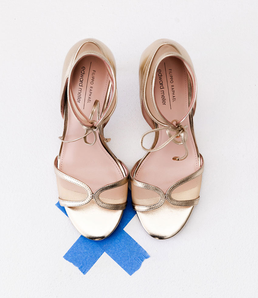 Gold high-heeled sandal with thin straps on a light gray background