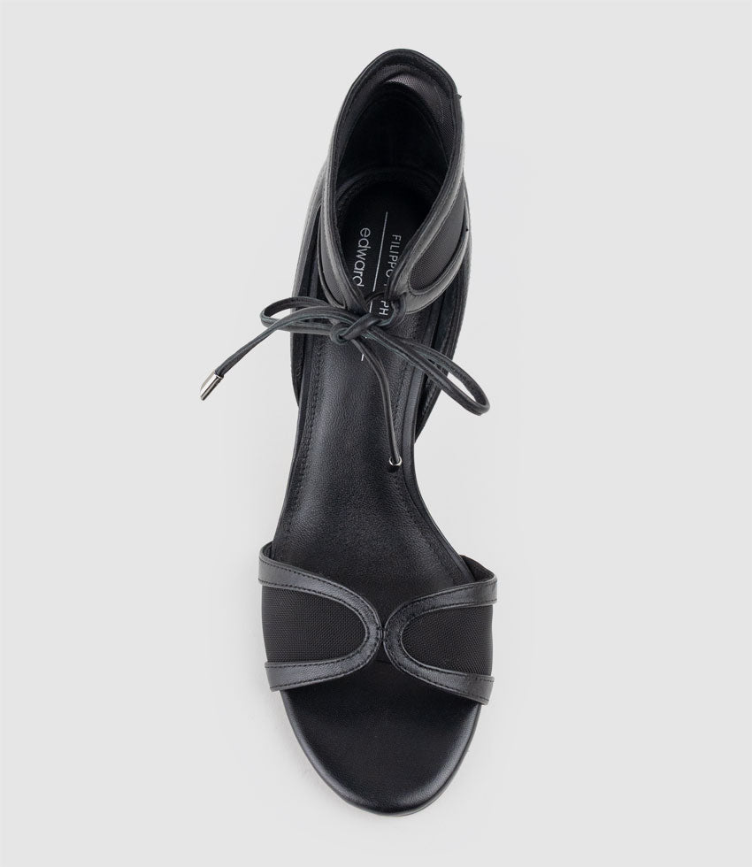 Black sandal with thin straps on a light gray background