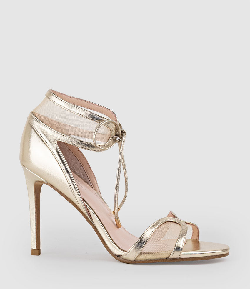 Gold high-heeled sandal with thin straps on a light gray background