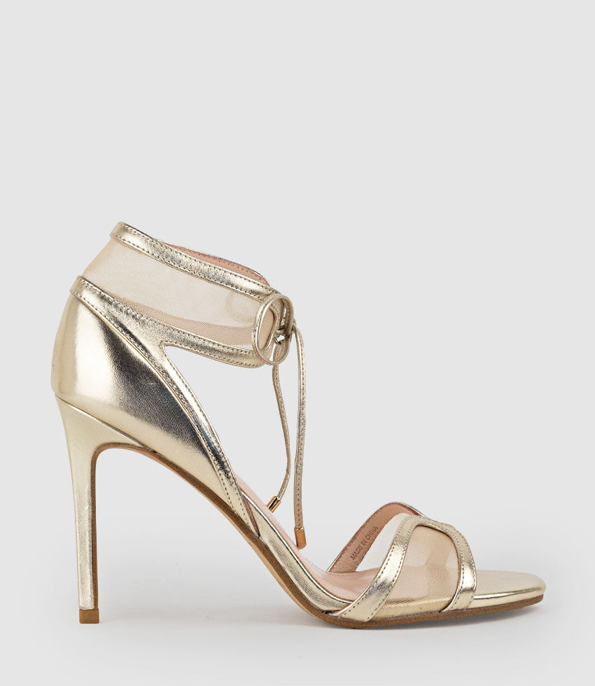 Gold high-heeled sandal with thin straps on a light gray background